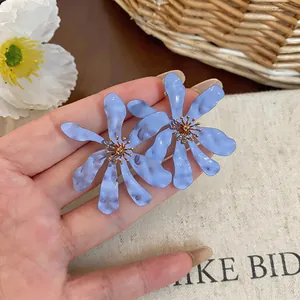 Macro dettaglio di grandi orecchini a fiore blu pieghettato con dettagli in oro