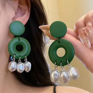 Primo piano di orecchini circolari in legno verde con nappine di perle su modella.