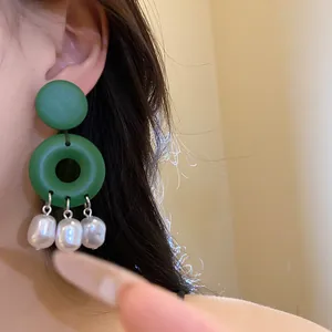 Primo piano di orecchini in legno verde con nappe di perle barocche indossati.