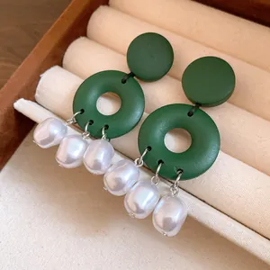 Dettaglio di orecchini tondi in legno verde con nappine di perle bianche in scatola.