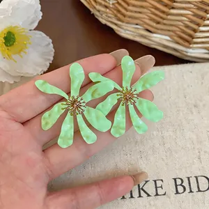 Dettaglio di orecchini a fiore in smalto verde chiaro plissettati tenuti in mano