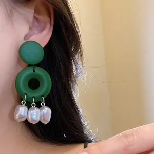 Dettaglio di orecchini a cerchio in legno verde con nappe di perle barocche