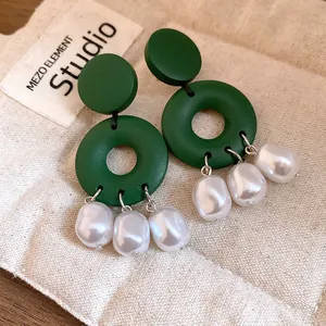Dettaglio macro di orecchini in legno verde con eleganti nappe di perle bianche.