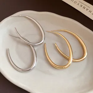 Vista ravvicinata di orecchini a cerchio ovali in oro e argento su piatto di ceramica