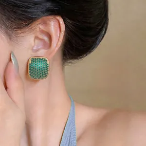 Detailed close-up showing elegant gold square earrings with green zircon stones on model's ear