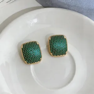 Close-up view of elegant geometric gold earrings featuring vibrant green pave stone inlay