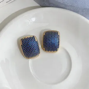Close-up of elegant gold geometric stud earrings with blue zircon paving.
