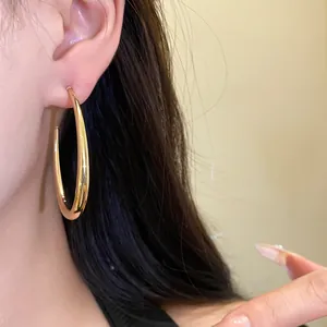 Primo piano di eleganti orecchini a cerchio ovali placcati oro con finitura a specchio su modella
