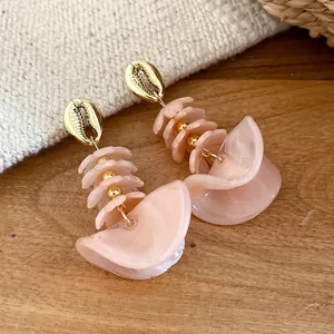 Elegante perzik acryl oorbellen met schelpontwerp en gouden accenten op houten basis