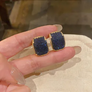 Macro view of geometric gold-tone stud earrings with pave-set sparkling blue cubic zirconia stones