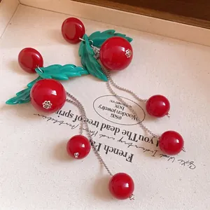Vintage cherry resin earrings with green leaves and long silver tassel chains on canvas.