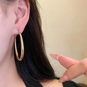 Primo piano elegante di un orecchino a cerchio ovale liscio dorato minimalista su orecchio.