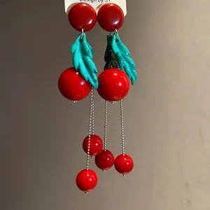 Close-up detail of retro cherry resin earrings with green leaves and tassel chain
