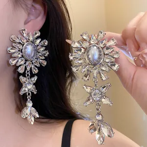 Close-up of glamorous oversized floral drop earrings with rhinestones and central pearl.