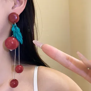 Close-up of retro cherry-themed resin earrings with teal leaf and silver tassels