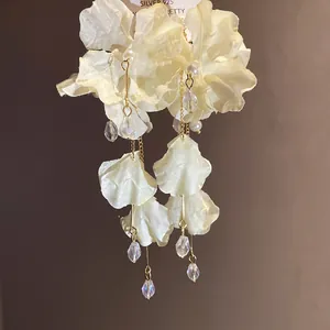 Vista dettagliata di lunghi orecchini a fiore in chiffon crema con perle e cristalli