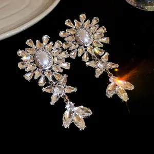 Close-up of sparkling flower drop earrings with oval pearls and clear crystals.