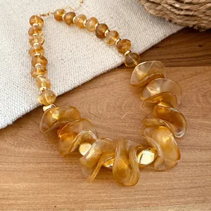 Detail van onregelmatige amberkleurige acrylkralen en gouden spacers op een retro ketting