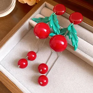 Close-up of vintage resin cherry earrings with green leaves and silver tassels