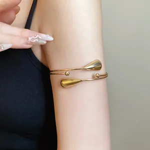 Close-up detail of a minimalist gold-tone double-layer metal arm cuff with teardrop design