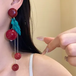 Detailed view of retro red resin cherry earrings with green leaf and long tassels