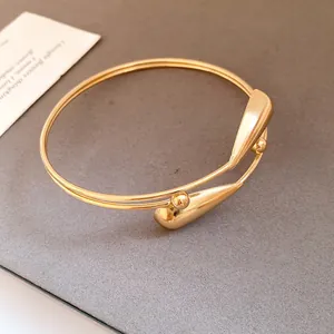 Detail view of a double-layered gold open bangle with teardrop ends on a textured gray background