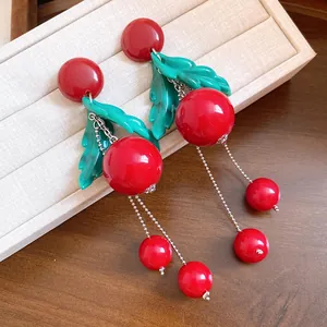 Close-up of cherry earrings with red resin beads and green leaves on a jewelry tray.