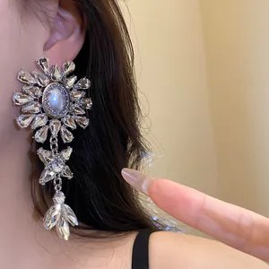 Close-up of oversized silver flower chandelier earrings with rhinestones and faux pearls.