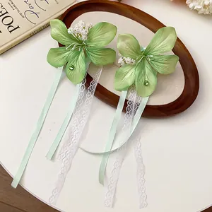 Pair of elegant green fabric flower hair clips with lace and ribbon tassels on a tray.