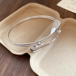 Close-up of silver double-layered open bangle with minimalist teardrop design.