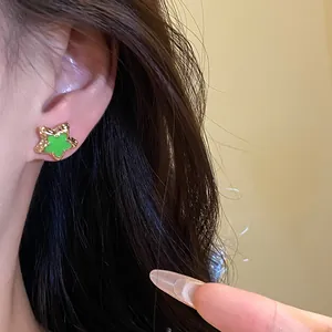 Detailed macro view showing a green enamel star stud earring worn on a female ear