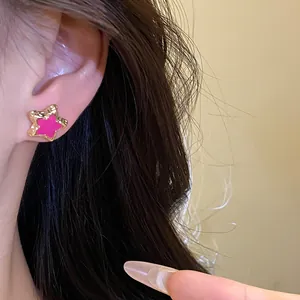 Detailed view of a sweet pink star stud earring with a gold-tone border worn on a person's ear