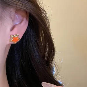 Close-up of a sweet orange star-shaped stud earring with gold-tone textured border.