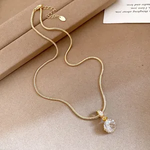 Detailed close-up of a gold snake chain necklace with a sparkling round zircon pendant.
