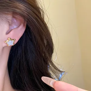 Detailed close-up view of a gold-toned star shaped stud earring with white inlay on ear