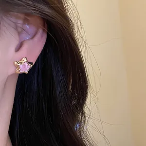 Detailed view of sweet pink star stud earring with gold-plated frame worn on ear