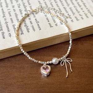 Elegant silver beaded bracelet featuring a pink heart crystal, pearl, and bow charm on a book