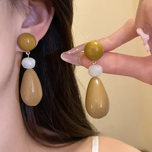 Detailed view of resin teardrop earrings with brown and white beads on model's ear