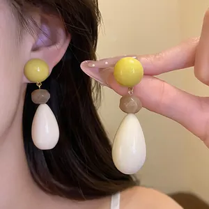 Detailed view of vintage resin teardrop earrings in yellow and white, worn by a model