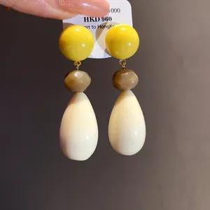 Macro detail of resin teardrop earrings with yellow round studs and silver needles