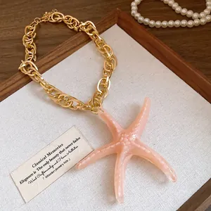 Macro view of a gold chain necklace with a large pink acrylic starfish pendant.