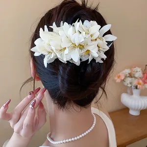 Close-up of white fabric flower hair clip with dewdrop beads on a bun hairstyle.