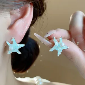 Close-up of elegant starfish pearl stud earrings worn and held to show detail