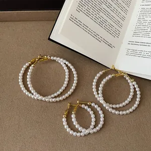 Eleganti orecchini a cerchio con perle bianche in tre misure su un libro vintage.