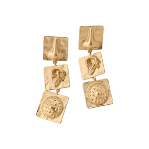 Surrealist gold drop earrings with artistic nose and ear designs on square plates.
