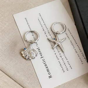 Close-up of asymmetrical silver earrings featuring starfish and seashell with pearls