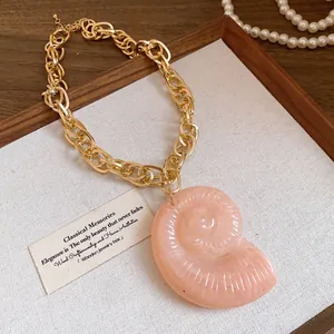 Detailed view of pink acrylic conch shell pendant on a vintage chunky gold chain necklace.