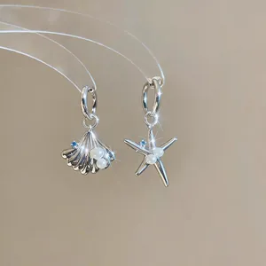 Detailed view of asymmetric shell and starfish earrings with pearls and blue zircons.