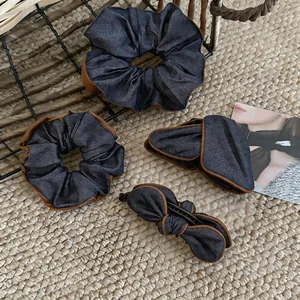 Set of deep blue denim-textured hair scrunchies and clips with brown piping on woven mat