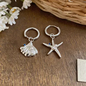 Detail view of asymmetric silver earrings with starfish, seashell, pearls and blue zircon.